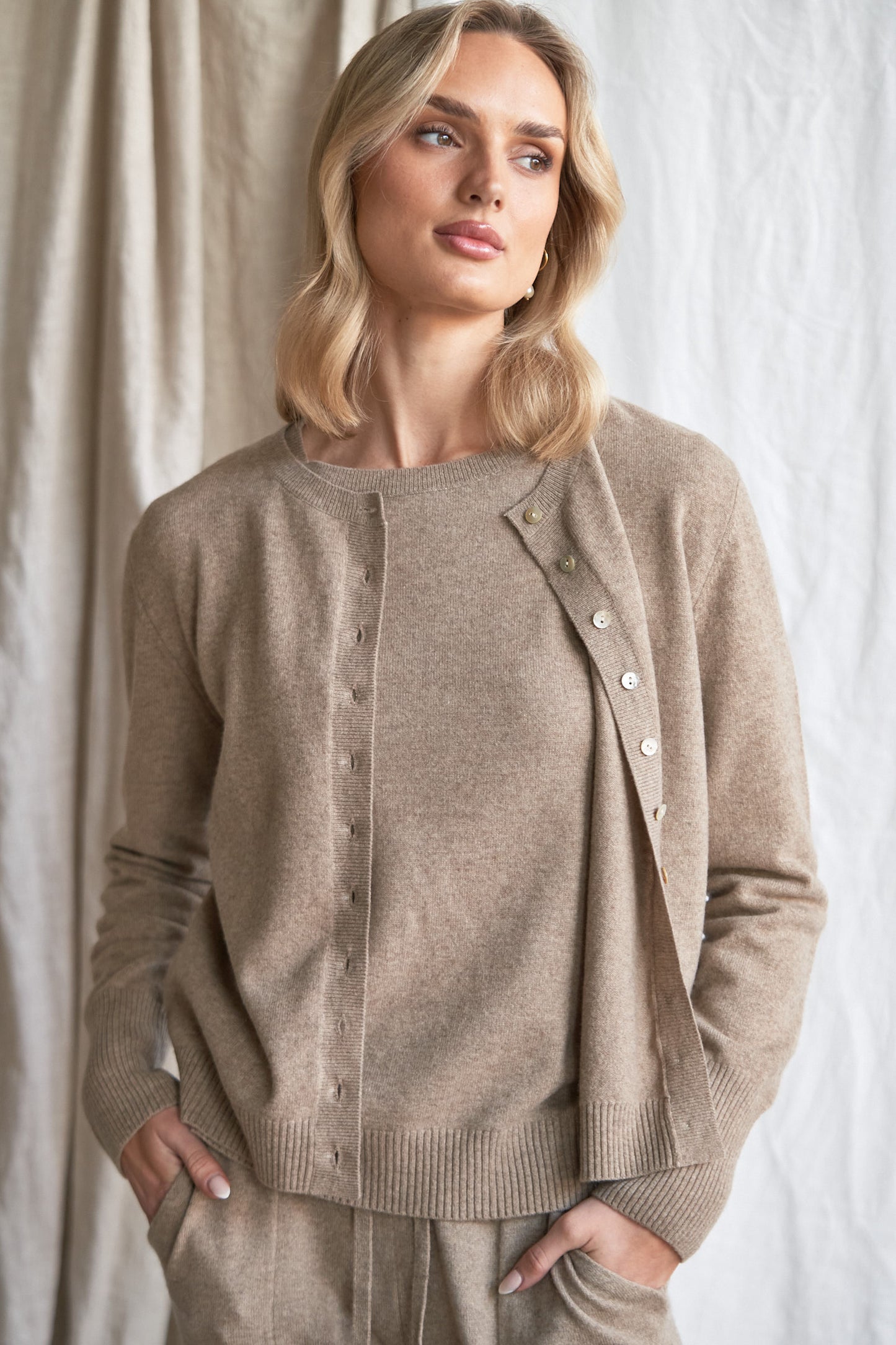 Mushroom Cashmere Cardigan – Women’s Knitwear with Mother-of-Pearl Buttons | 100% Pure Cashmere
Refined and versatile, our mushroom cashmere cardigan is a wardrobe essential for cool weather layering. Made from 100% ethically sourced pure cashmere, this women’s knit features a soft neutral taupe-grey hue and is finished with natural mother-of-pearl buttons for a delicate, elevated touch.
With a relaxed fit and luxurious softness, this cardigan is ideal for work, weekends, or travel. Lightweight yet warm,